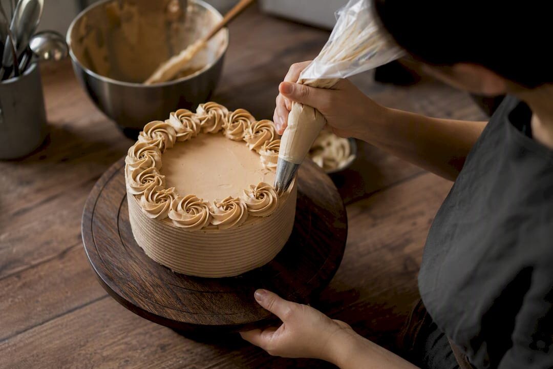 Hands piping rosettes on cake on turntable