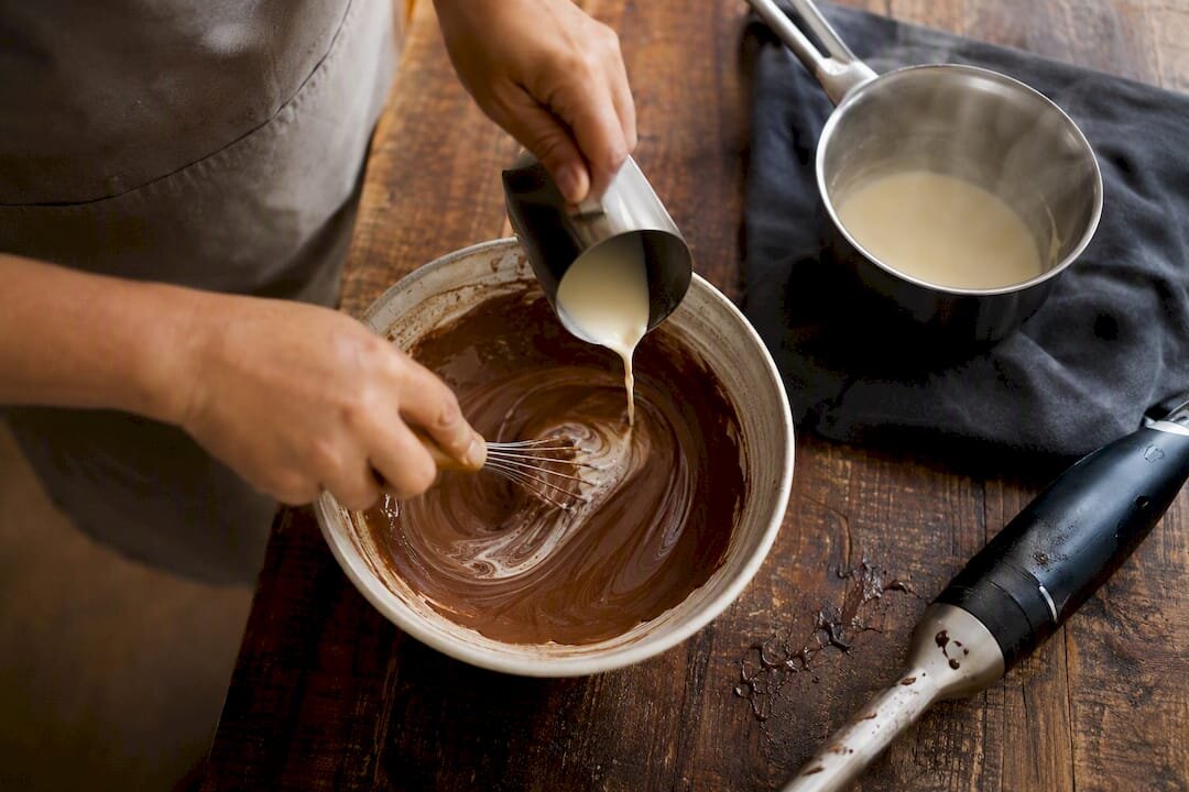 Hands fixing broken ganache with cream and whisk