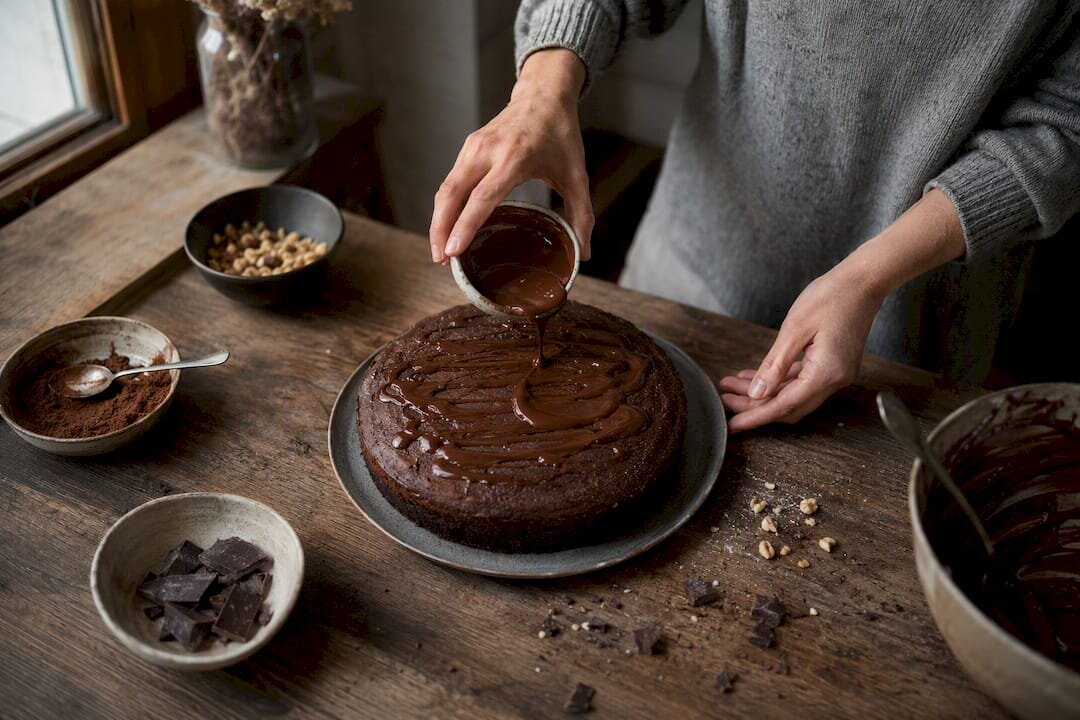 Hands finishing chocolate cake with cocoa powder